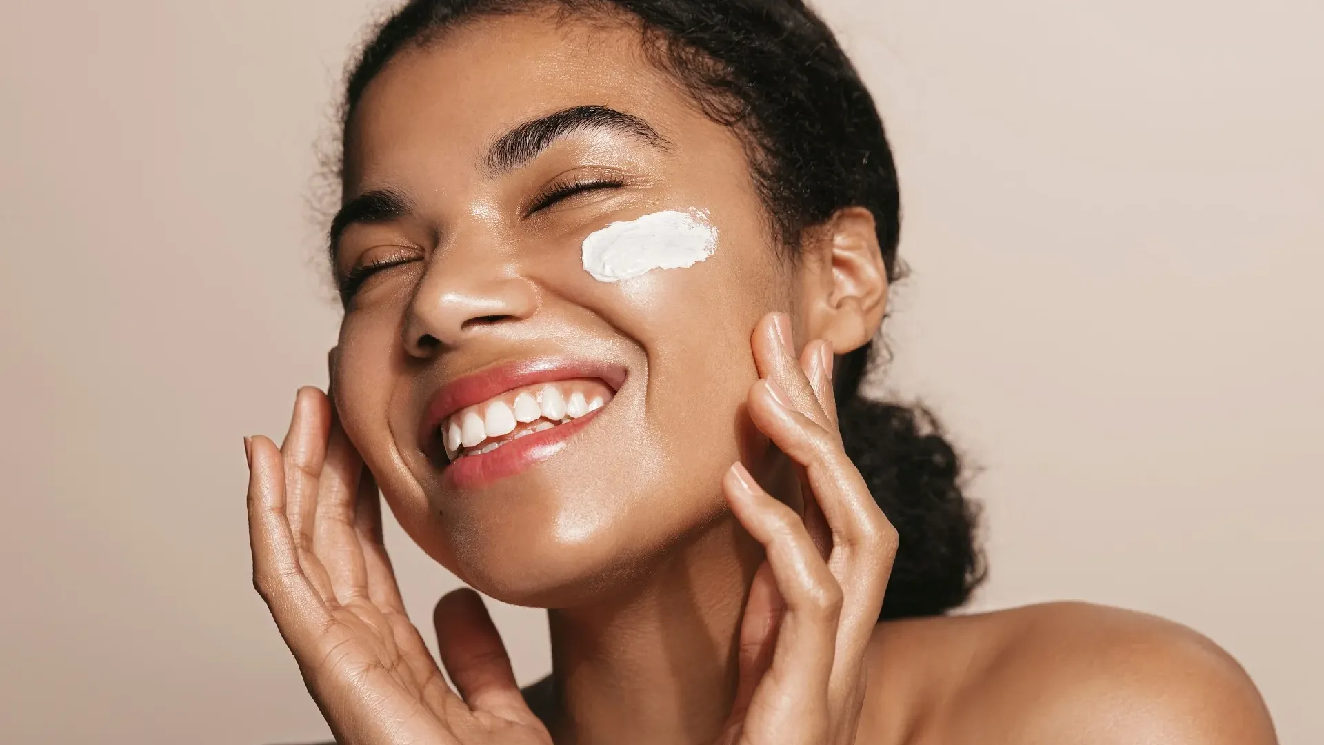 A joyful woman with Osmosis Skincare cream on her cheek.