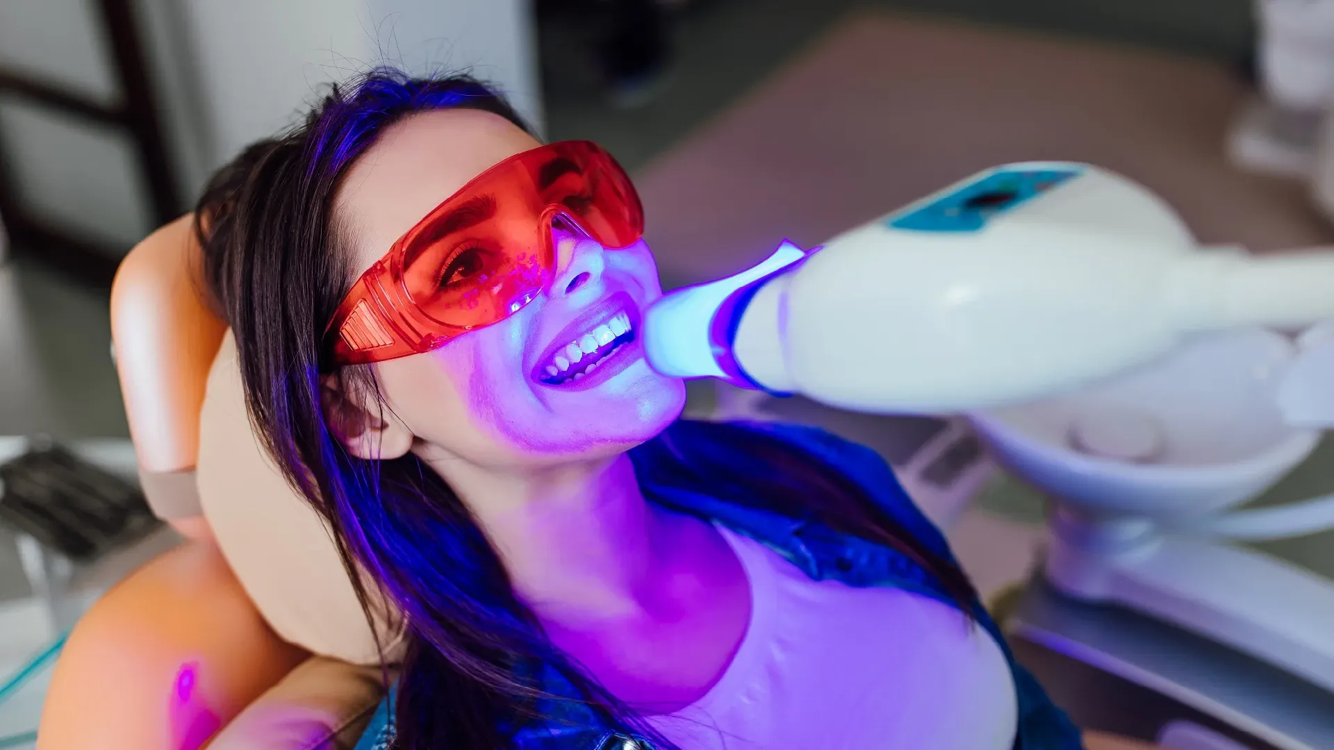Woman undergoing teeth whitening procedure with a laser and protective eyewear.