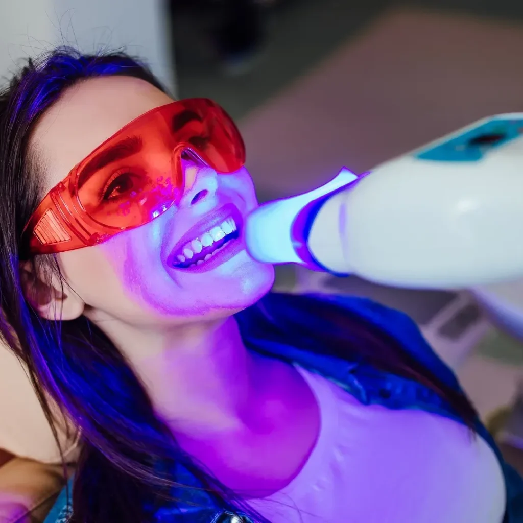 Woman undergoing teeth whitening procedure with a laser and protective eyewear.